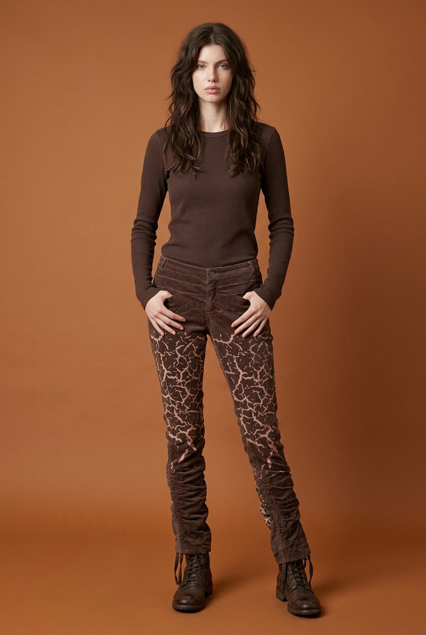 Woman wearing a brown long-sleeve top and brown corduroy patterned pants against a rust colored background
