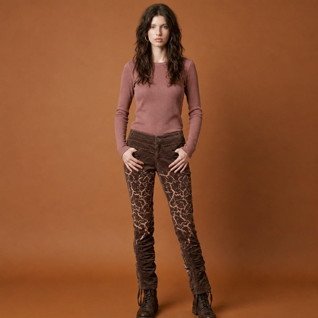Woman wearing a rose colored sweater and brown corduroy patterned pants against an rust background