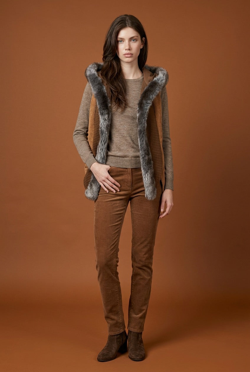 Woman wearing a brown outfit with a faux fur-trimmed vest in corduroy against an orange background