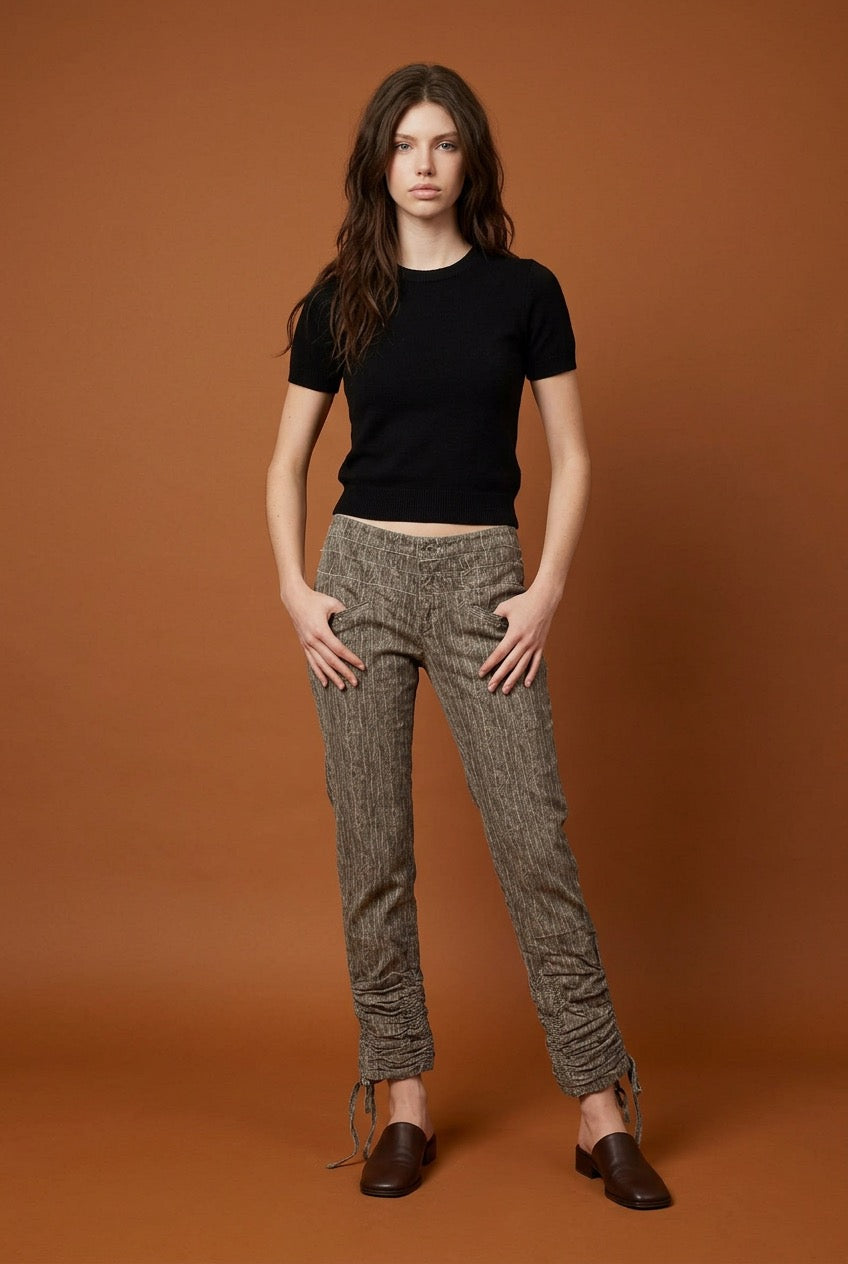 Woman wearing a black t-shirt and grey corduroy patterned pants against a brown background