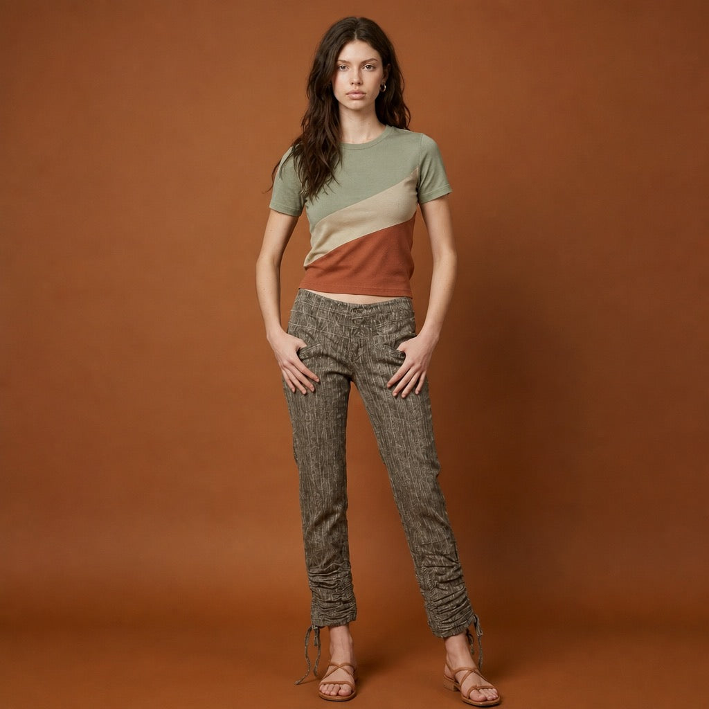 Woman wearing a color-blocked shirt and grey corduroy patterned pants on a brown background