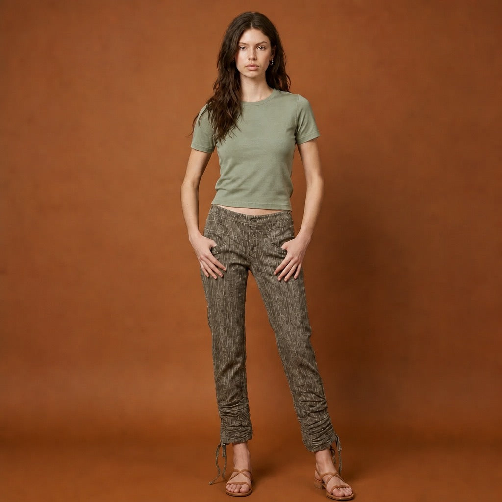 Woman wearing a green t-shirt and grey corduroy patterned pants against a brown background