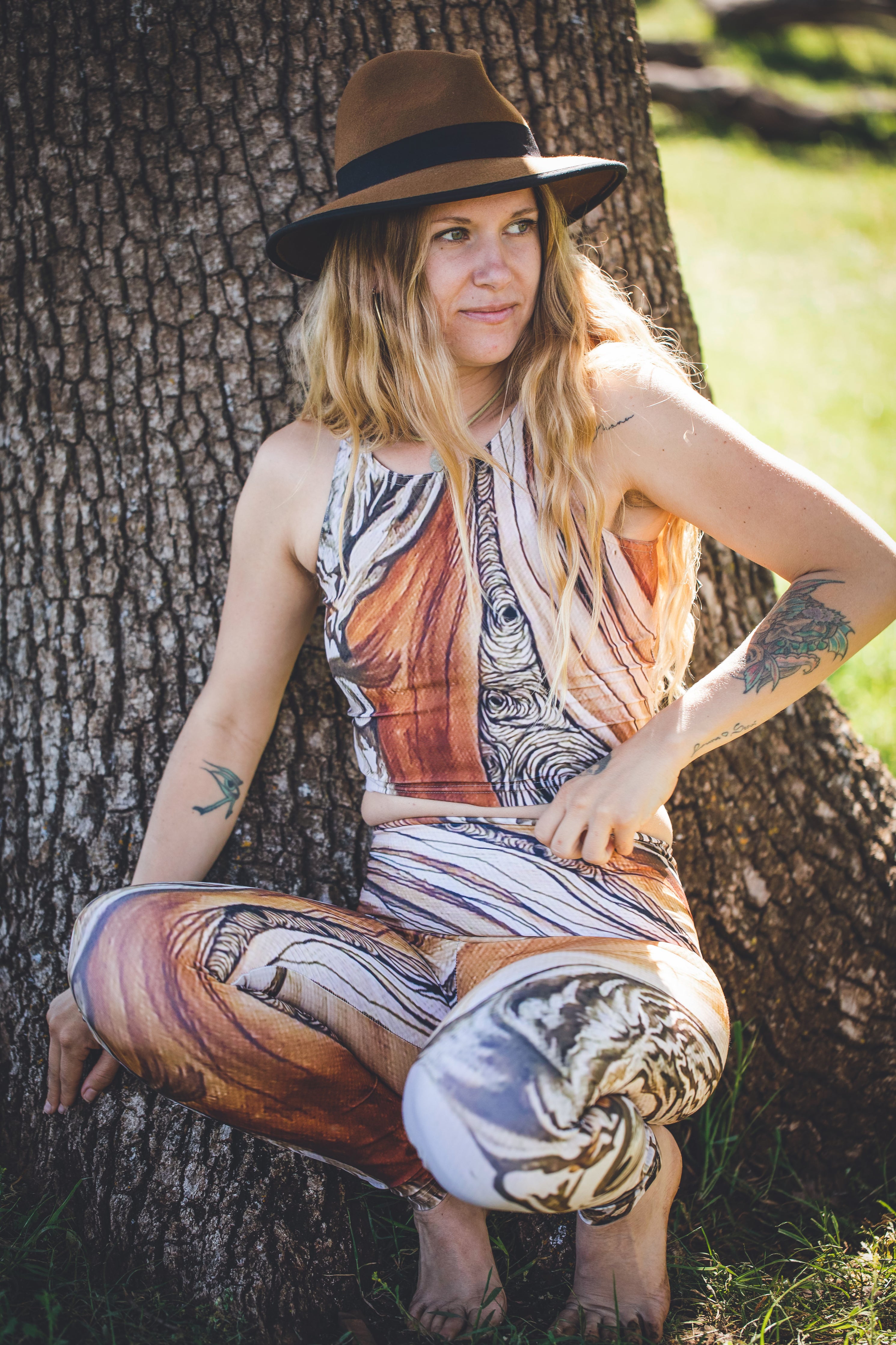 A person wearing a colorful leggings with a tree and line pattern, posing by a tree.